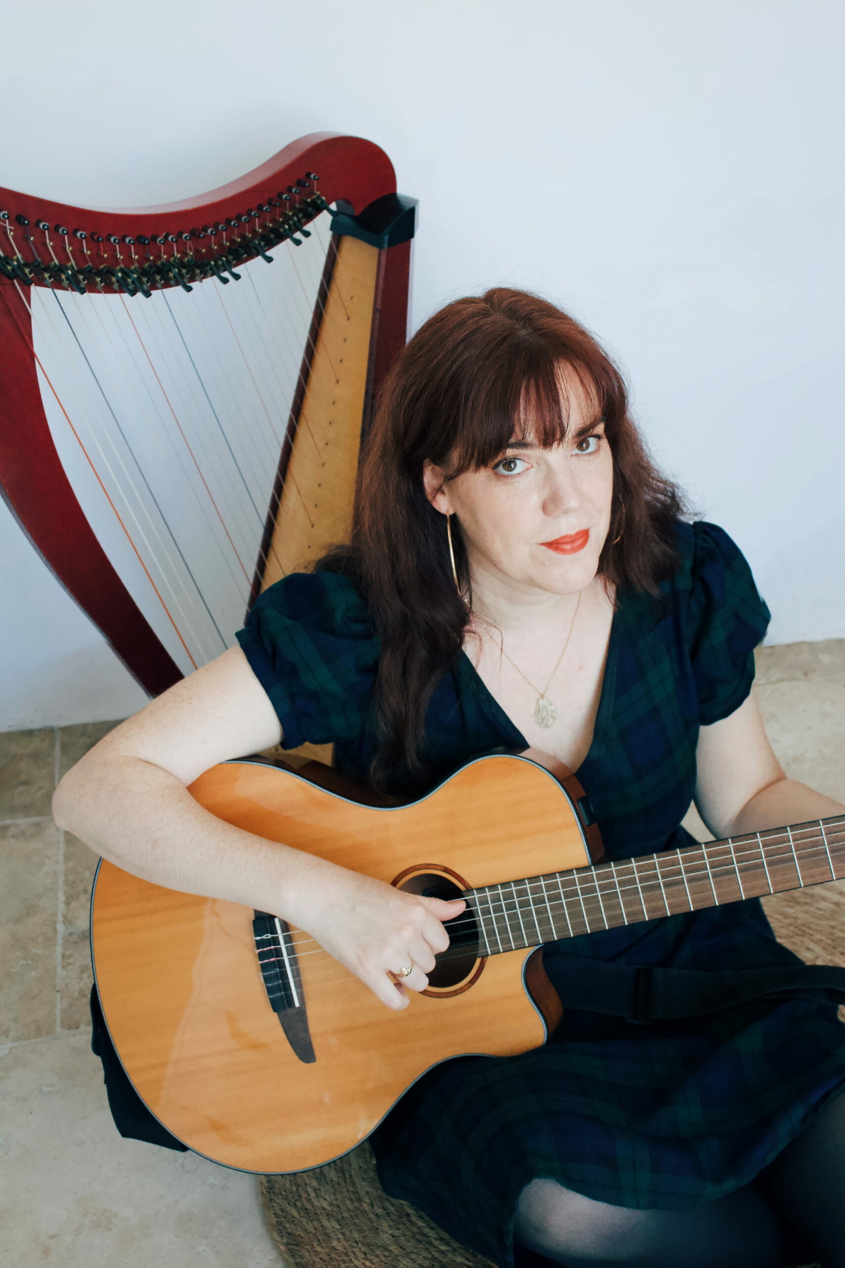 Jeanne Le Penglaou joue de la guitare. Il y a une harpe celtique derrière elle.